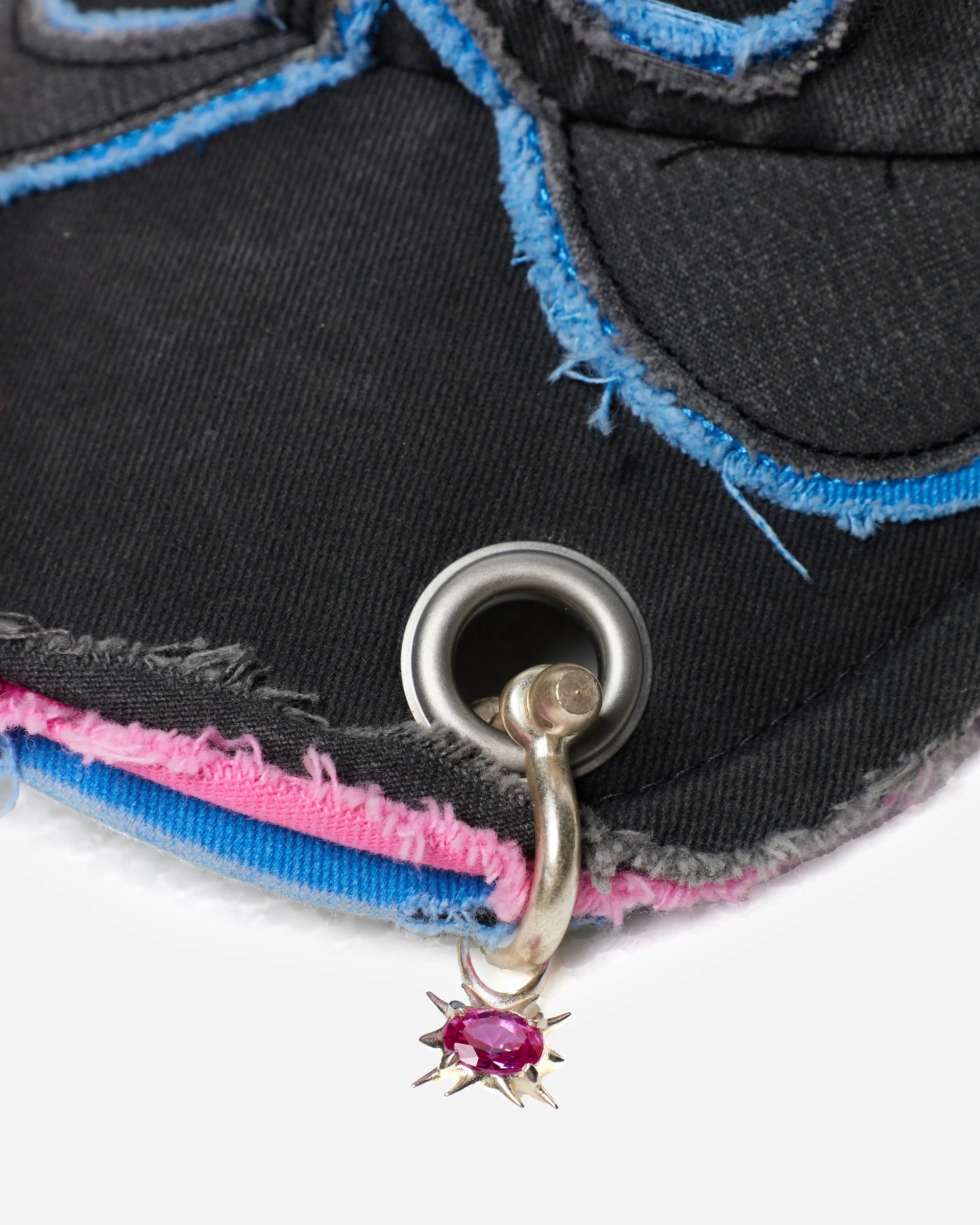 Close-up of a black fabric patch with pink and blue edges and a metal grommet with a star-shaped charm.