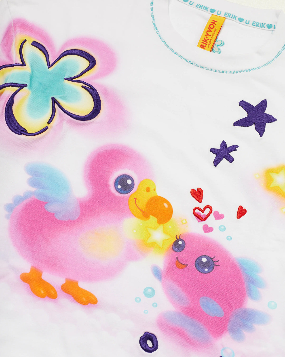 A close-up of a white t-shirt featuring colorful cartoon illustrations, including pink dodo bird and fish, yellow stars, purple stars, and red hearts. The brand slogan 'ERIK LOVE U' is printed repeatedly on the inner neck label.
