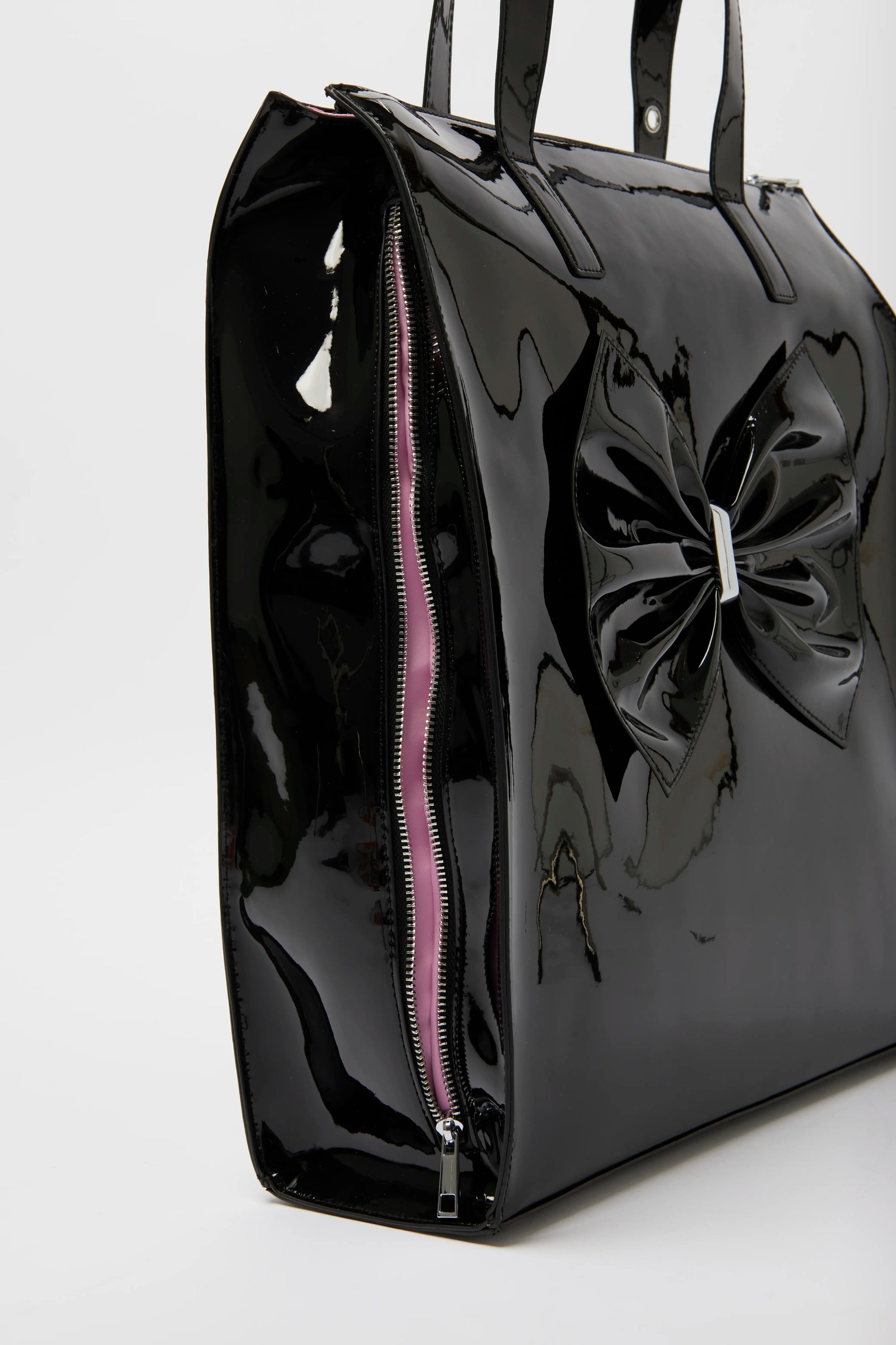 Oversized patent tote bag in black with a bow embellishment on the side, zipper closure, and a glossy finish.